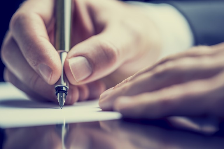 Close-up photo of someone's hands as they write with pen and paper